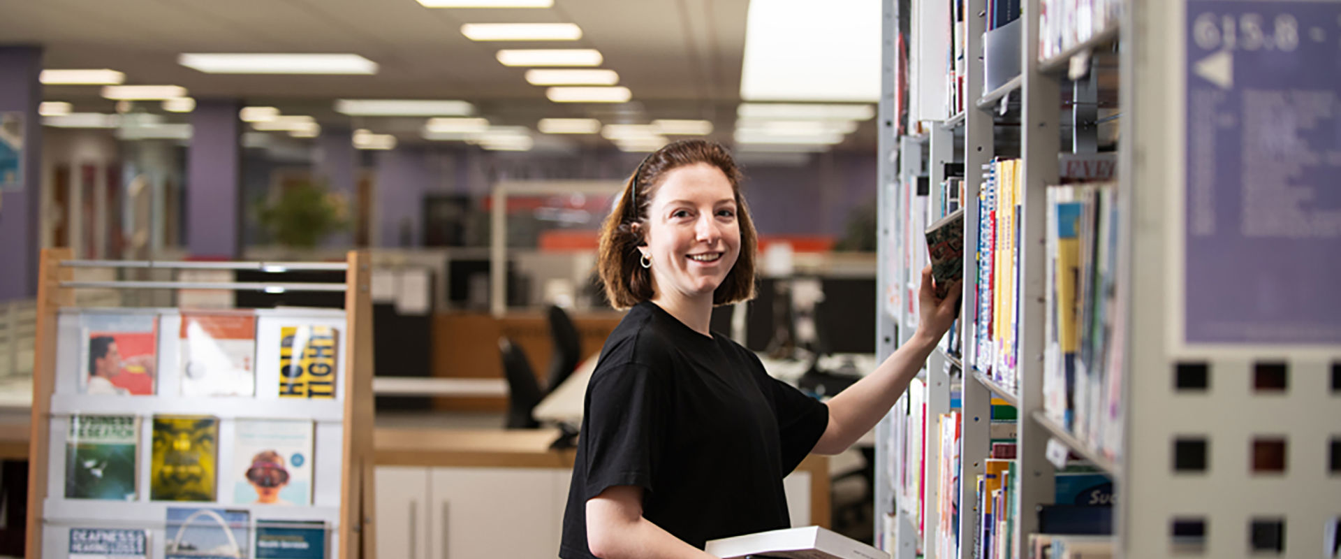Student picking out a book from a library shelf. 