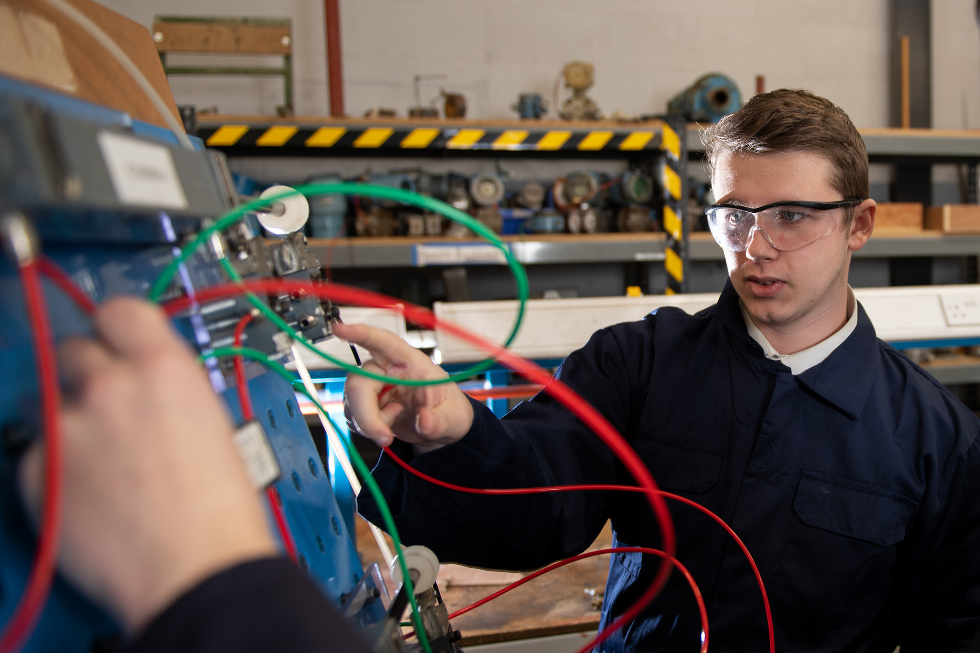 Student wearing safety goggles is working with green and red cables.