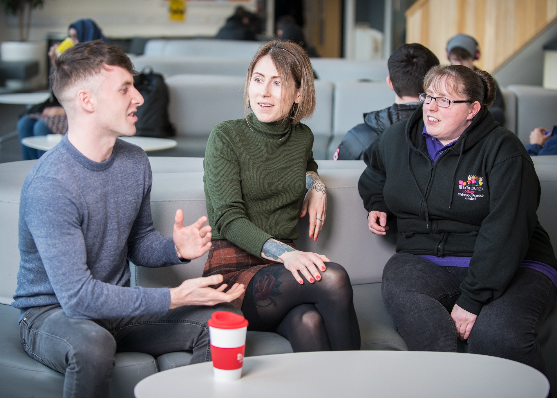 Three students having a conversation while sitting on a sofa at one of the college's communal areas.
