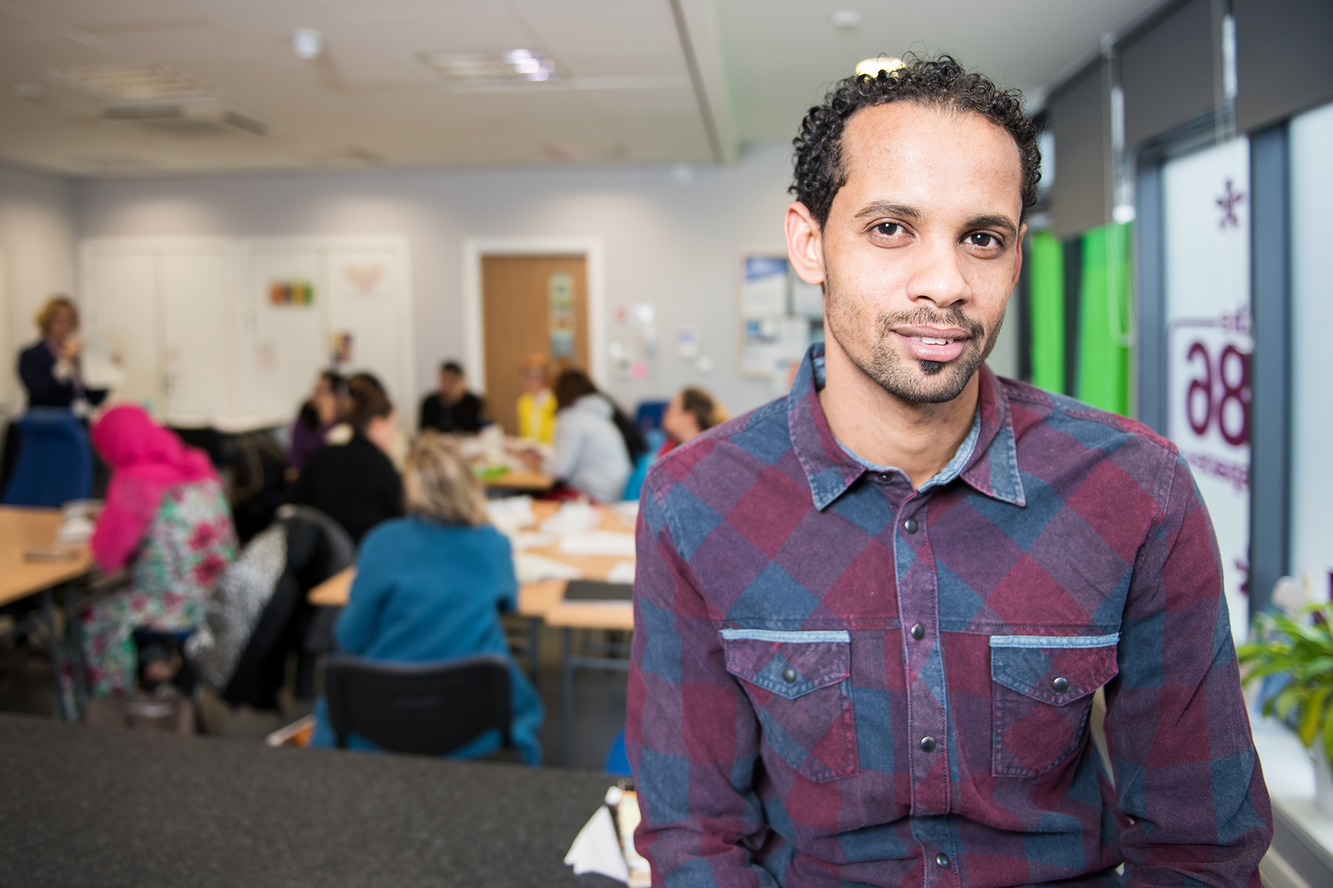 ESOL student smiling in their classroom as their peers work on tables behind.