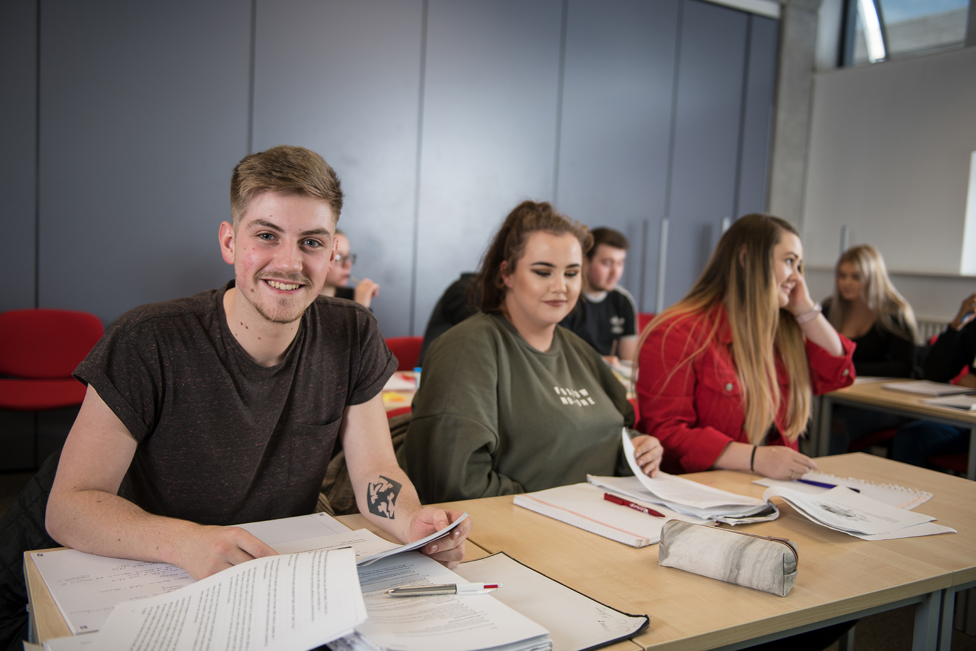 Social science students working on coursework at a desk in a classroom. 