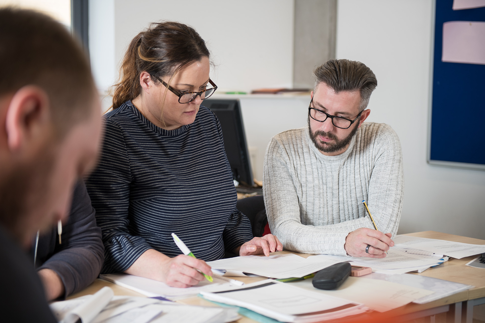 Enterprise and commerce students working together in a classroom, with papers and notes scattered over the desk.