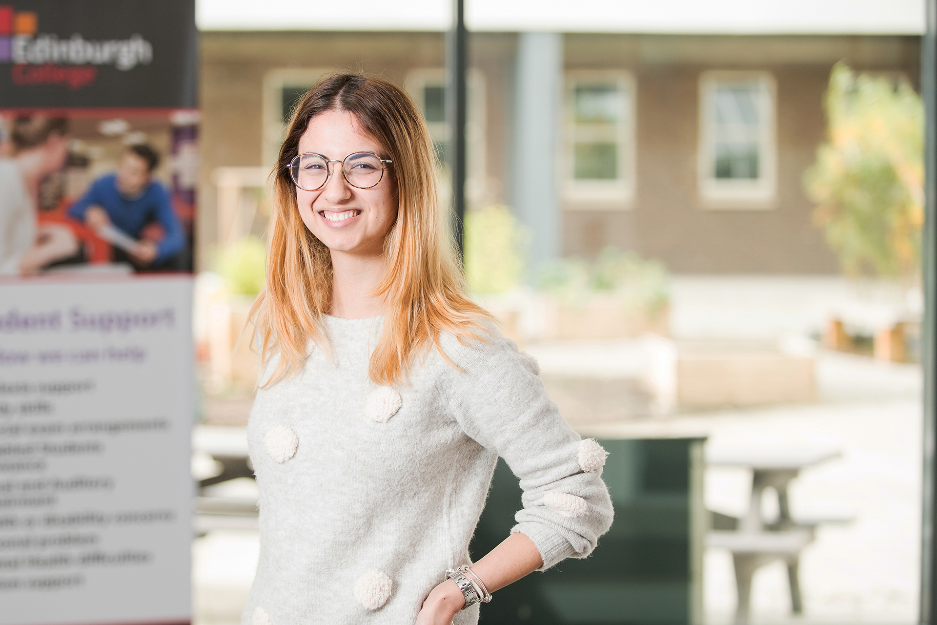 Smiling student wearing glasses in a college classroom.