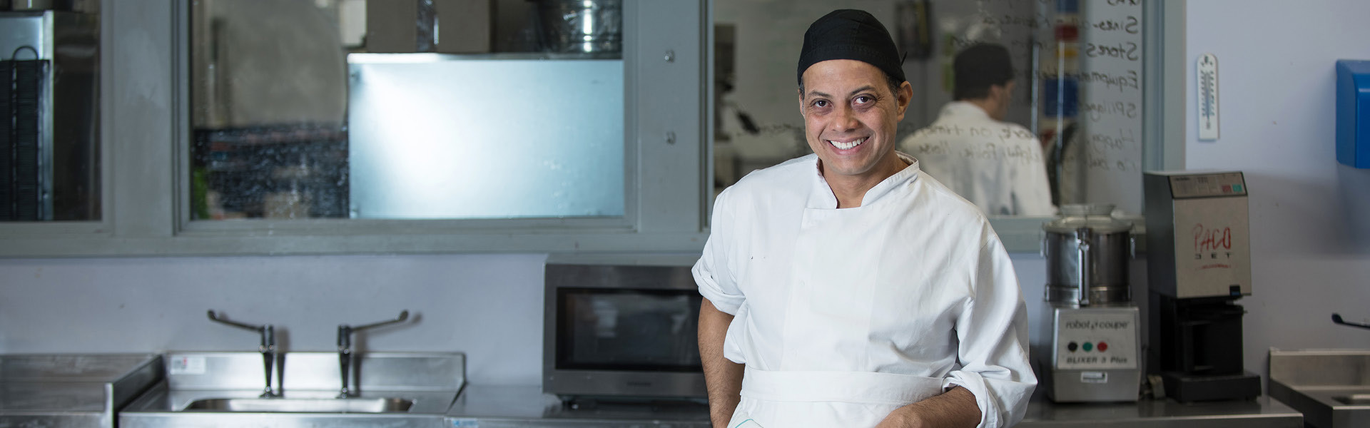 Cookery student wearing white uniform working in a kitchen.