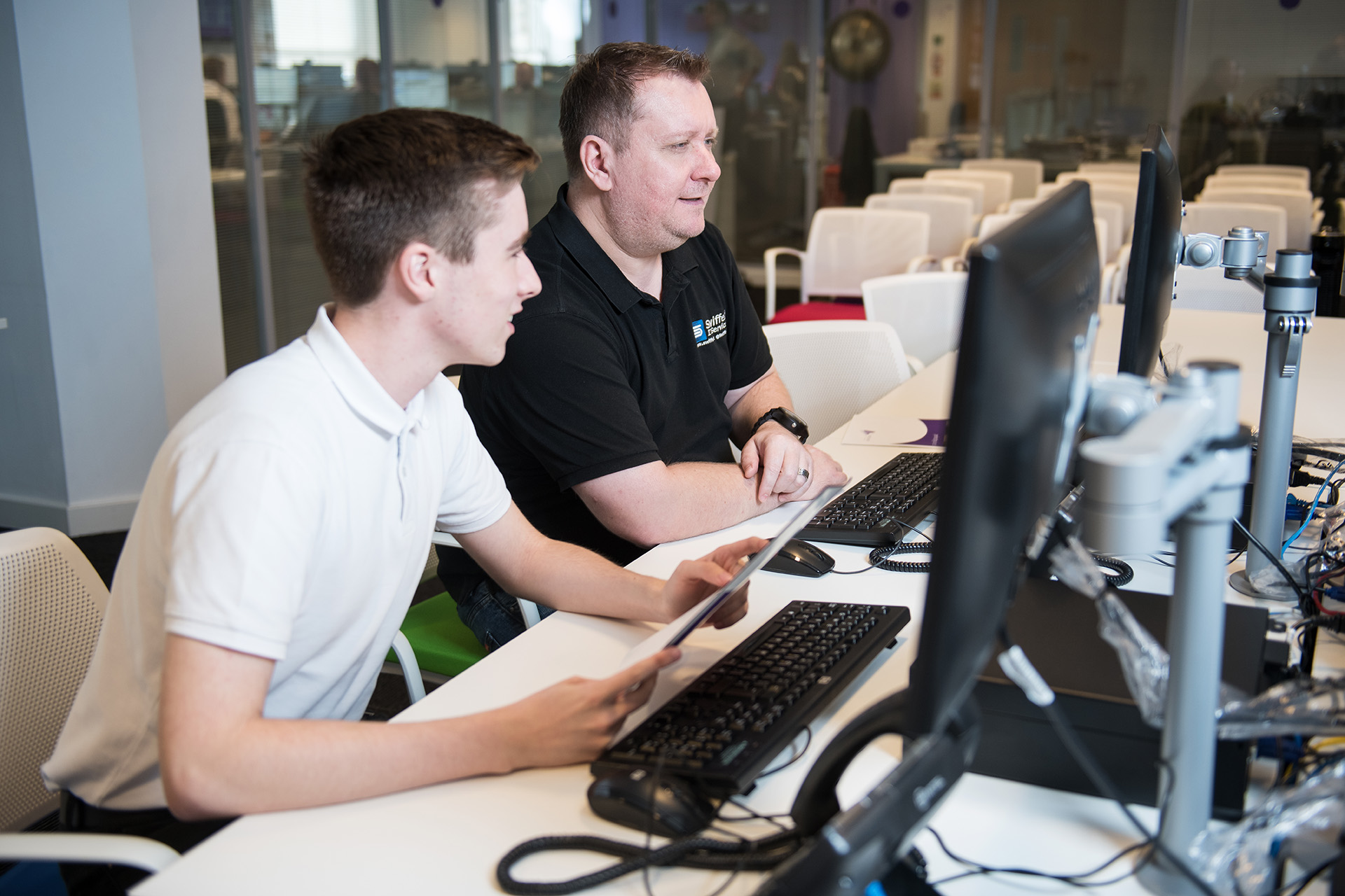 Young student working at a desk in an open plan office during a work placement next to their mentor.
