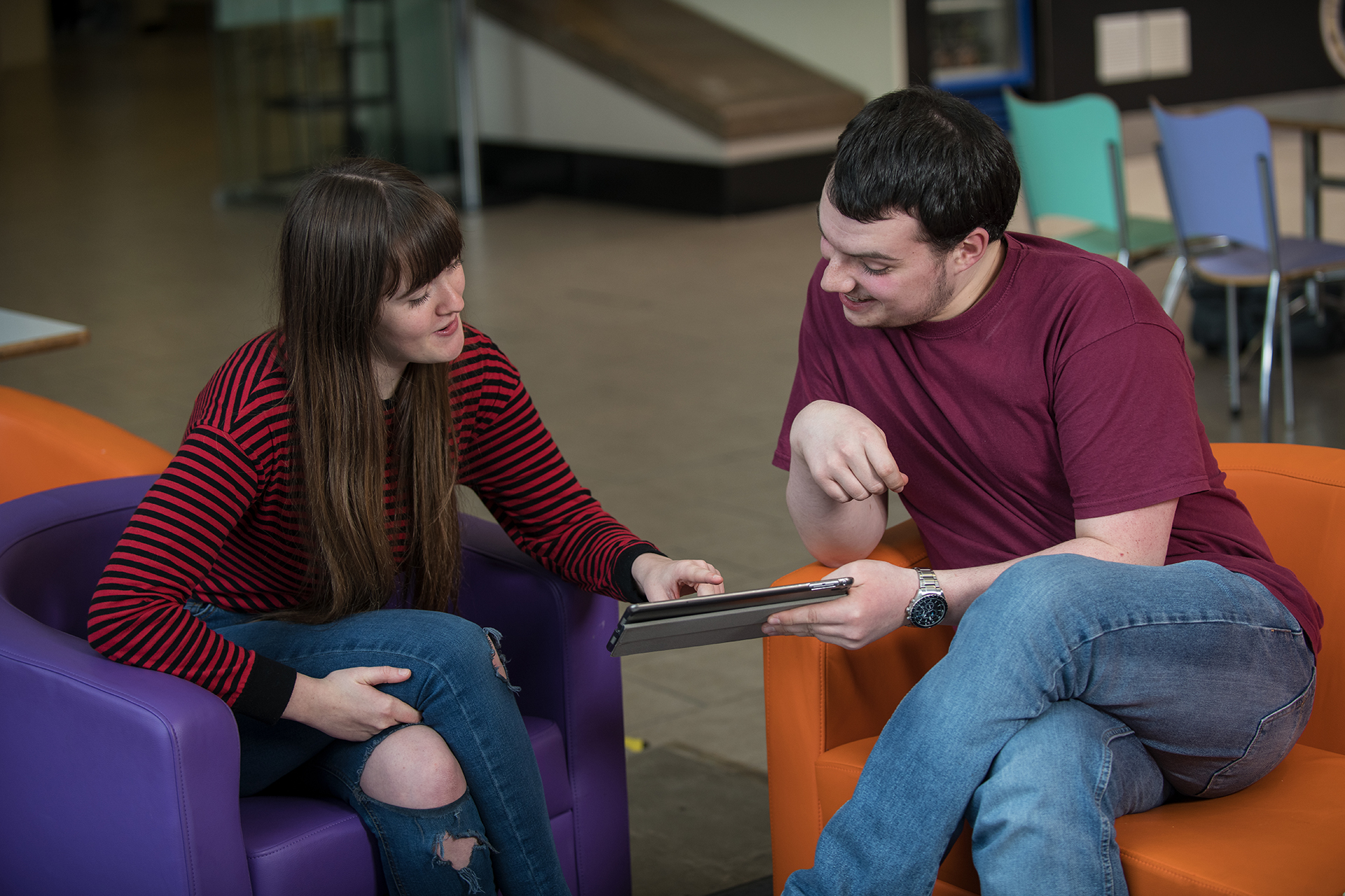 Two students talking about something while looking at something on their tablet screen.