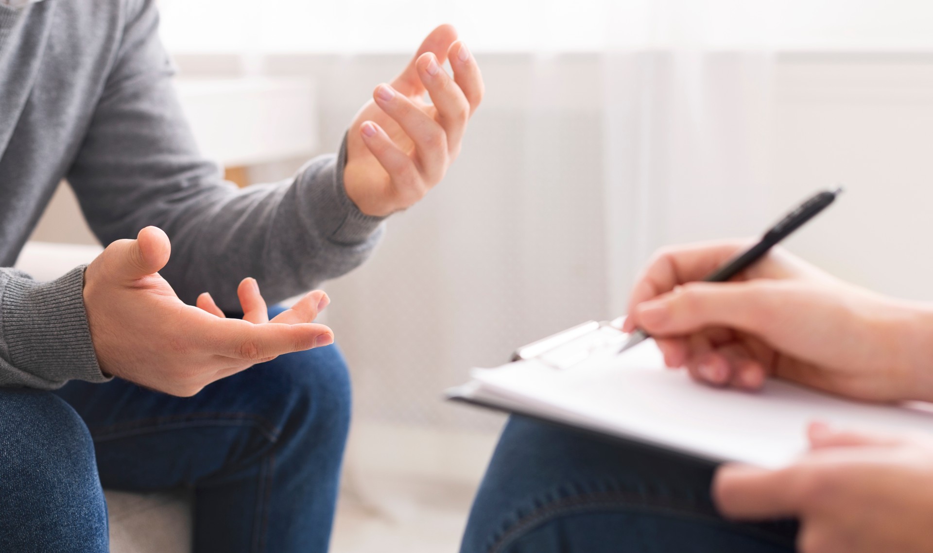 Close up of two people speaking during a counselling session. One person is taking notes on a notepad. 