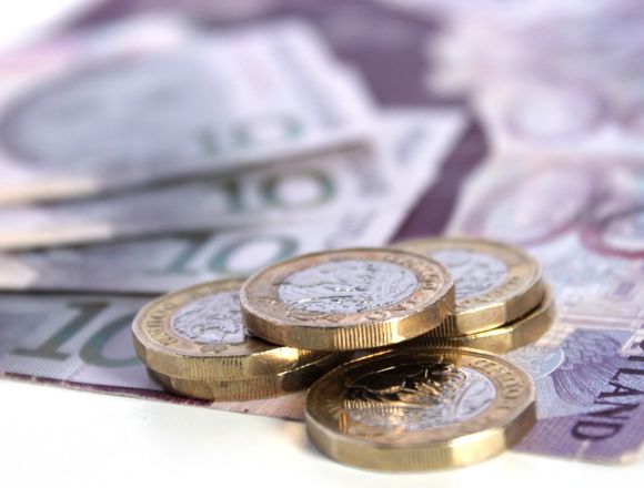 A stack of pound coins on top of bank notes.