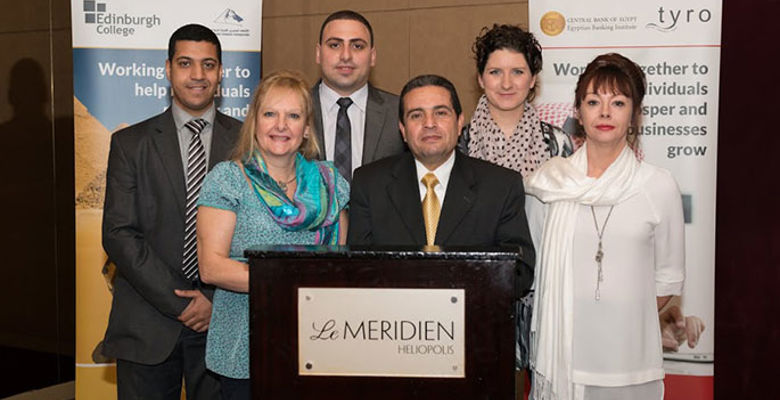 A group of six individuals posing for a photo, standing in front of a banner, with a podium in the foreground.