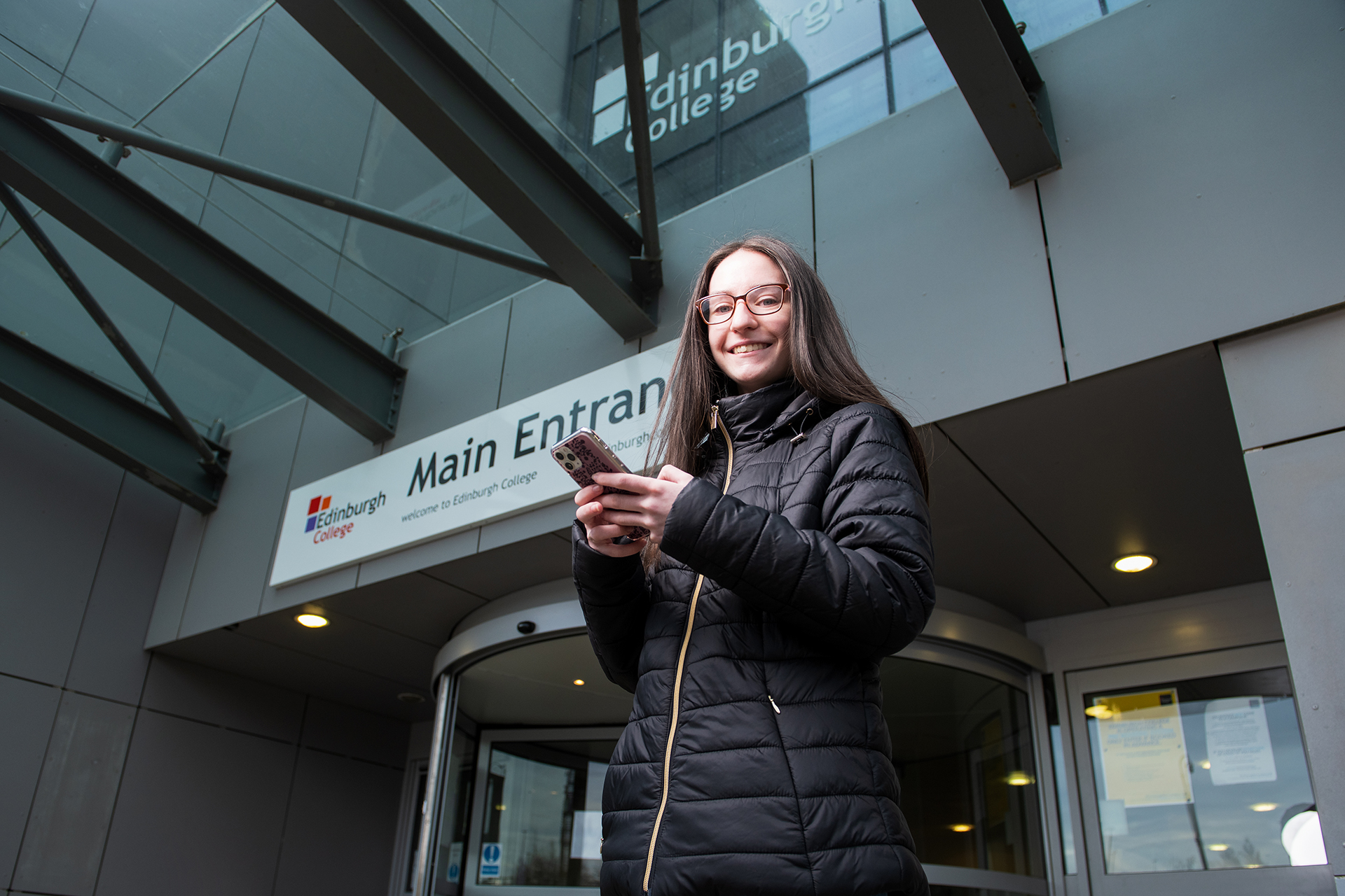 Young student looking at their phone outside a college campus building.