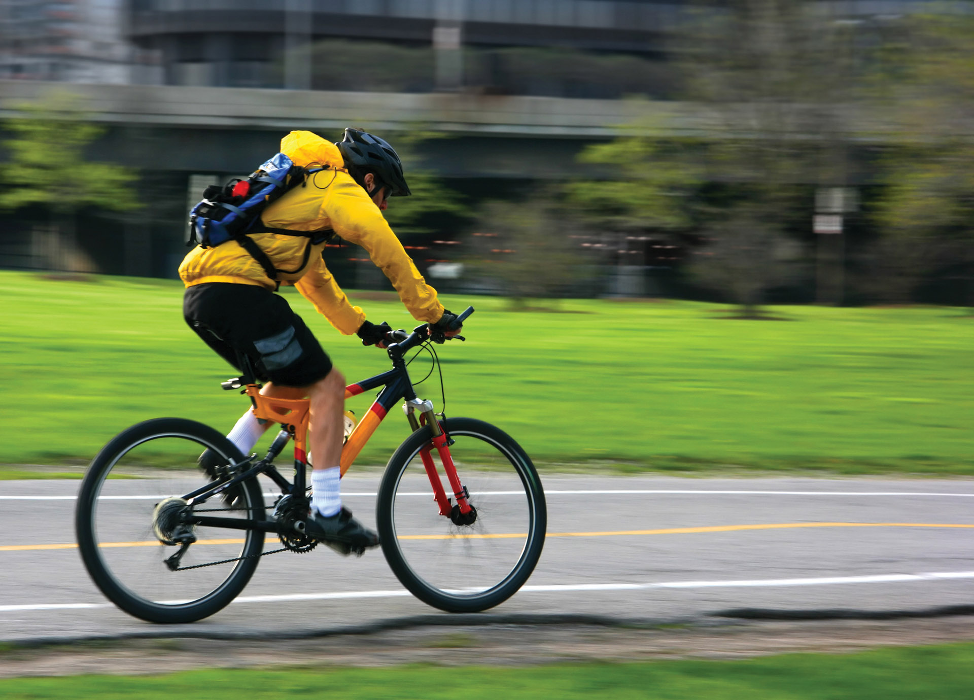 Student wearing a bright yellow jacket and helmet is cycling to college. 