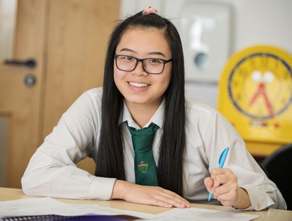 Smiling school pupil taking notes in a classroom.